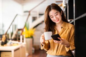 Young female holding coffee cup and smiling at phone